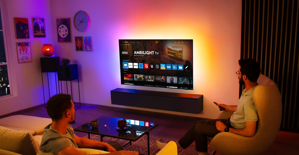 Dvaja muži sleduj&uacute; n&aacute;stenn&yacute; telev&iacute;zor Ambilight v ob&yacute;vačke